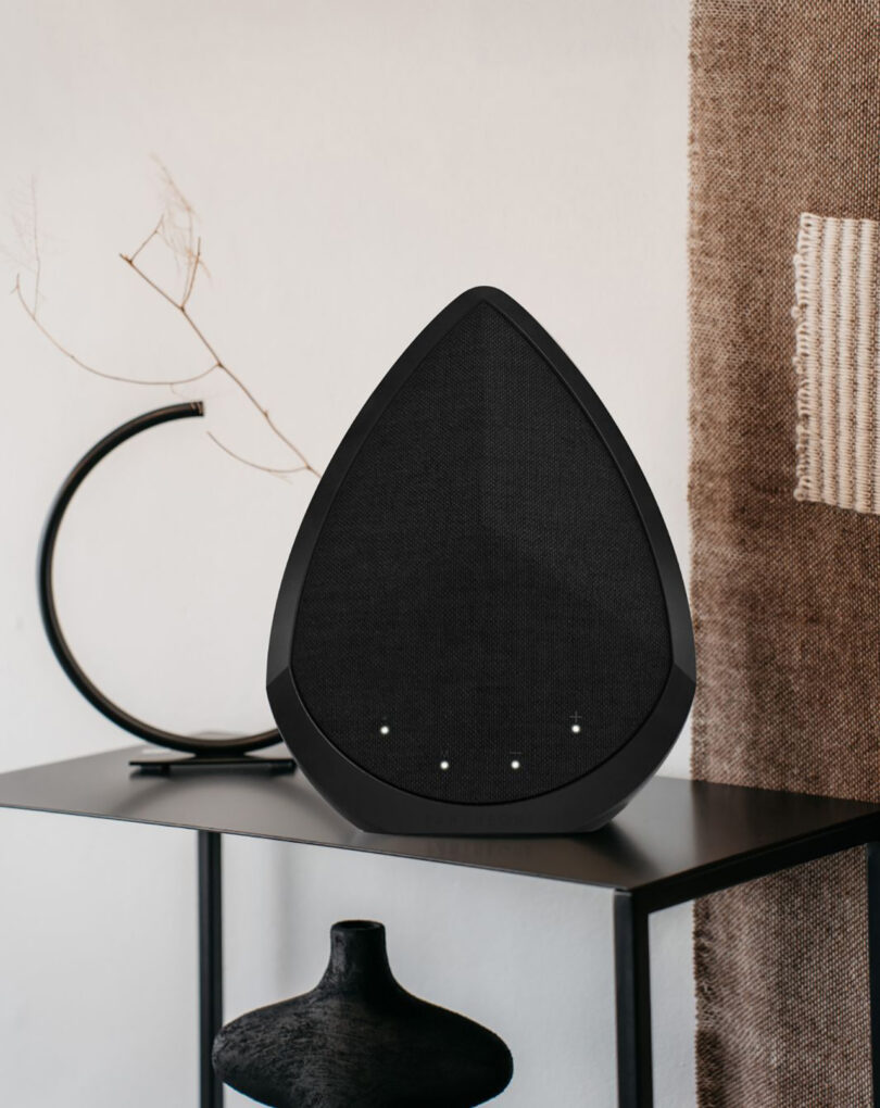 Pantheone Obsidian wireless speaker in black set within an organic modern decor setting on black metal shelf with tapestry in background.
