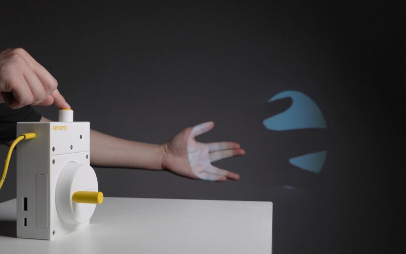 Person with one arm posed to create hand shadow in front of Narratron projector with other hand ready to press button to capture an image.