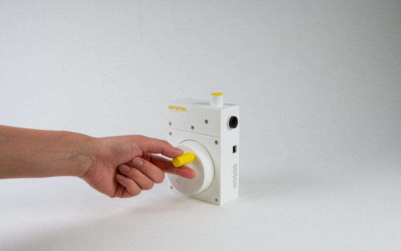 Person's arm reaching to manipulate Narratron projector with yellow hand crank dial.
