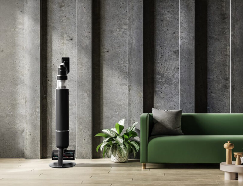 Samsung Bespoke AI stick vacuum in matte black set near green sofa near concrete walls.