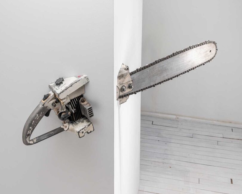 a sculpture of a real chainsaw breaking through a corner wall to the other side