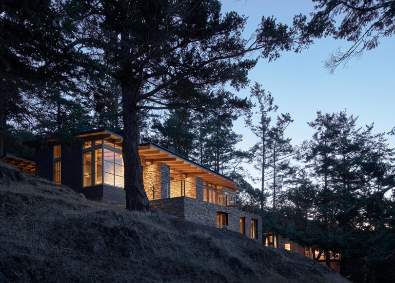 the facade of a home built into a hillside at dusk with lights lit within