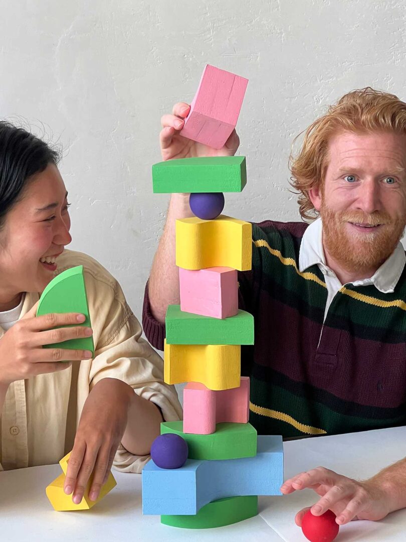 two people stacking brightly colored geometric blocks