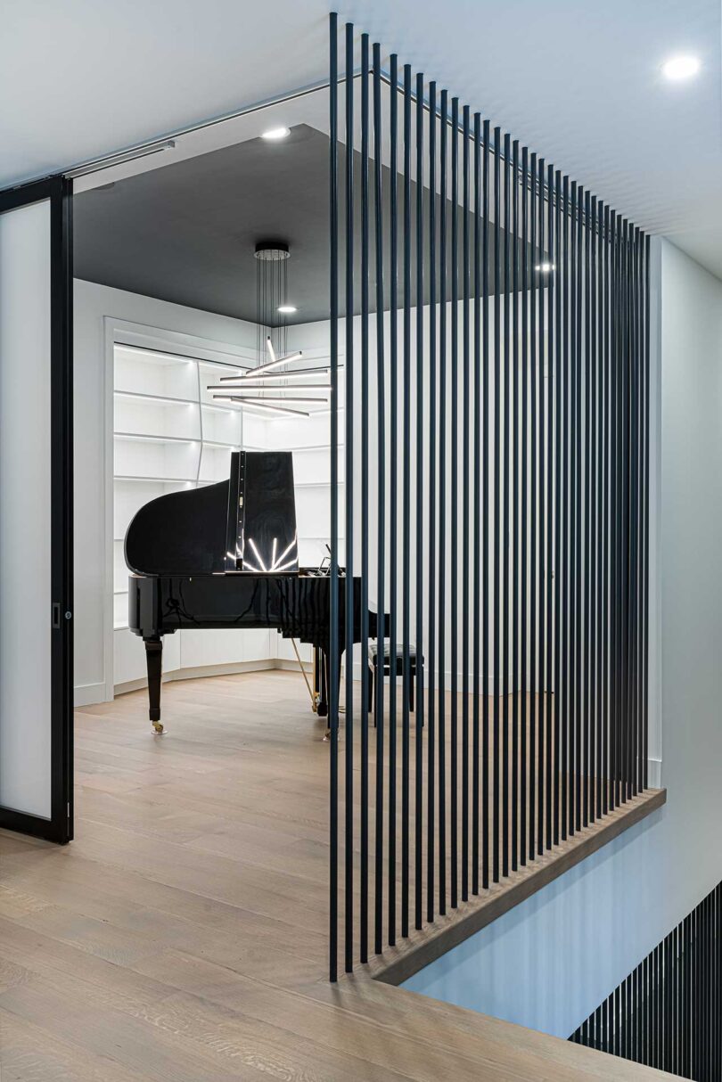 angled view into white room with black bars offering privacy with black grand piano 