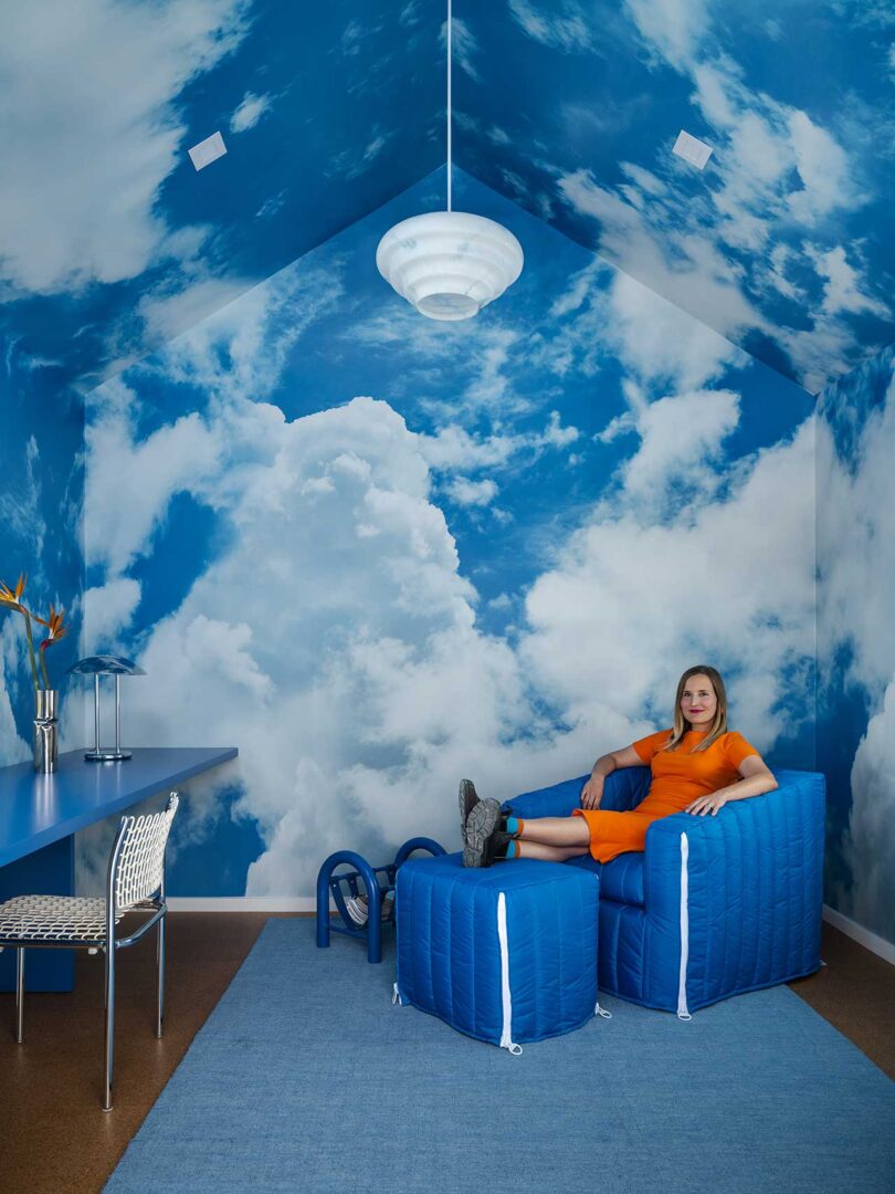 interior shot of room with cloud murals all over and person sitting in blue chair at end
