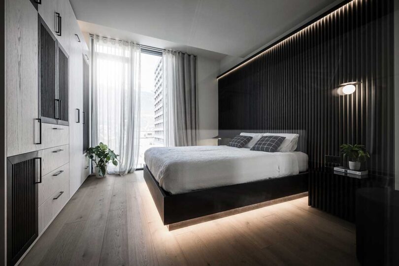 angled view of modern bedroom with black headboard wall with bed appearing to float with lights radiating from underneath