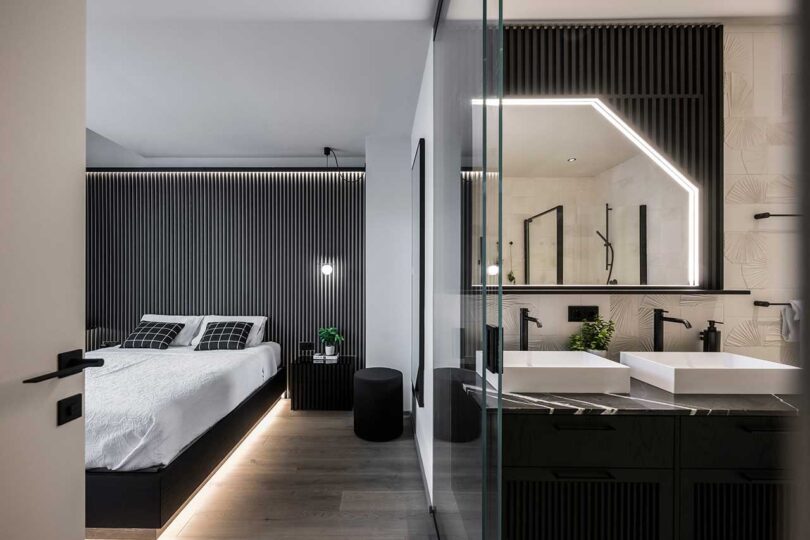 view of modern bedroom with black headboard wall with bed appearing to float with lights radiating from underneath split with partial view of modern bathroom