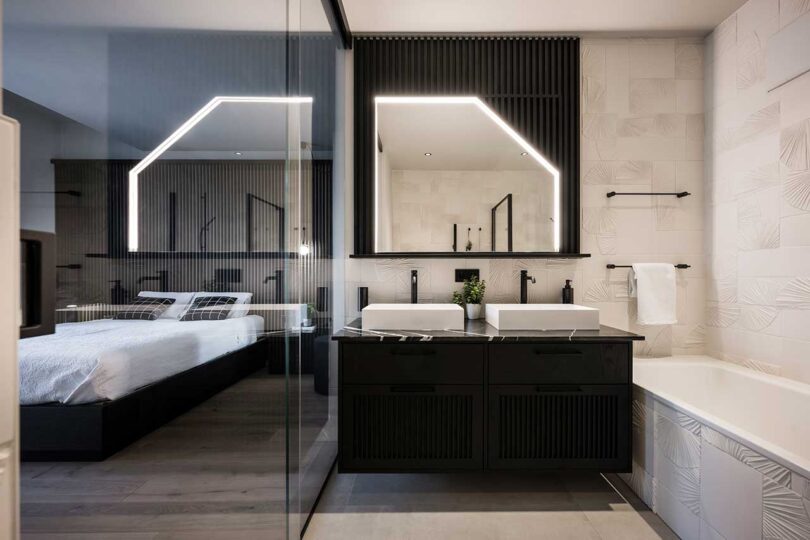 view of modern bedroom with black headboard wall with bed appearing to float with lights radiating from underneath split with partial view of modern bathroom