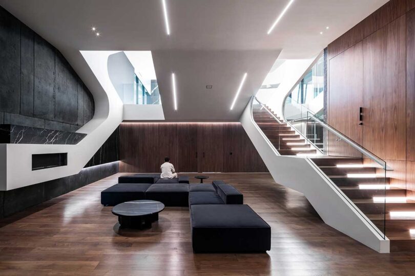 interior view of modern futuristic living room with large black modular sofa and wood stairs