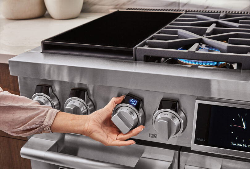 professional 48-inch stainless steel cooking range with a hand adjusting a burner knob to a precise temperature