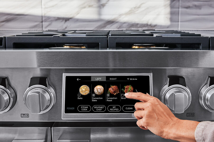 professional 48-inch stainless steel cooking range with a hand selecting a cooking feature on a touchscreen