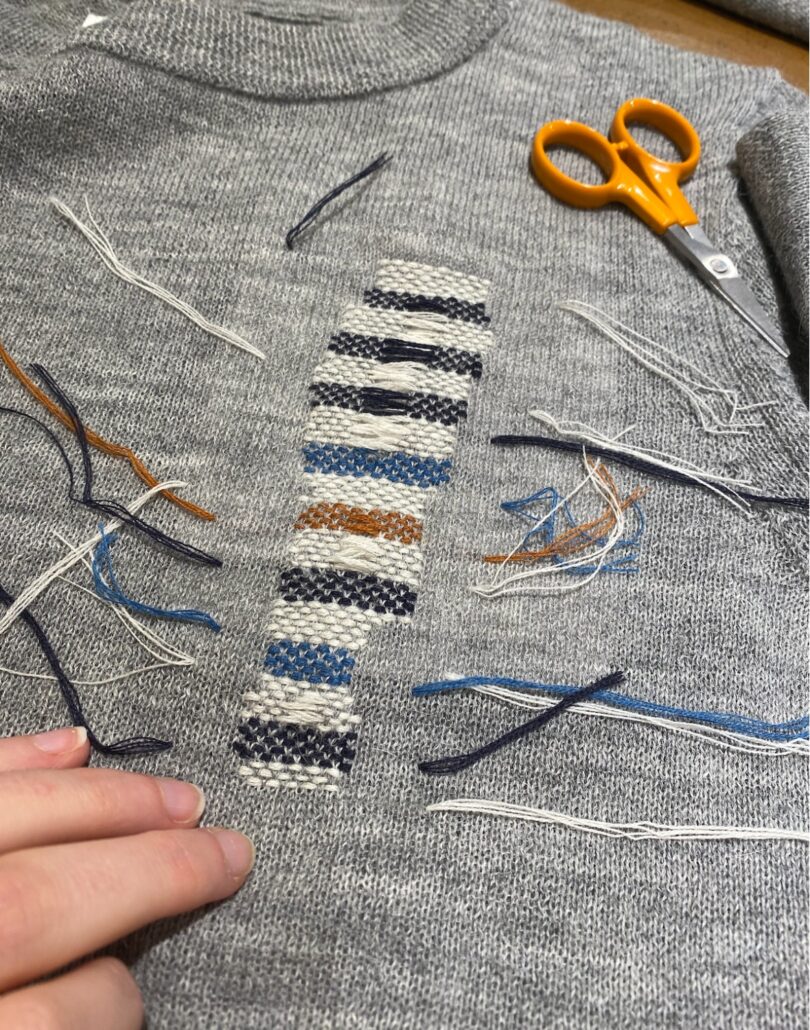 closeup of grey sweater with sewn design in different colored thread