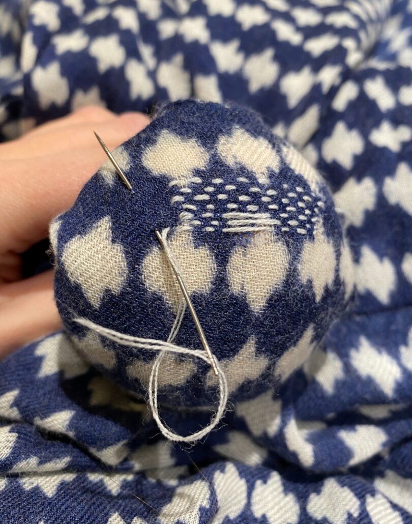 balled blue and white fabric with white thread sewn into linear pattern