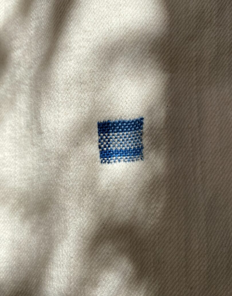 closeup of white fabric adorned with square of threaded design