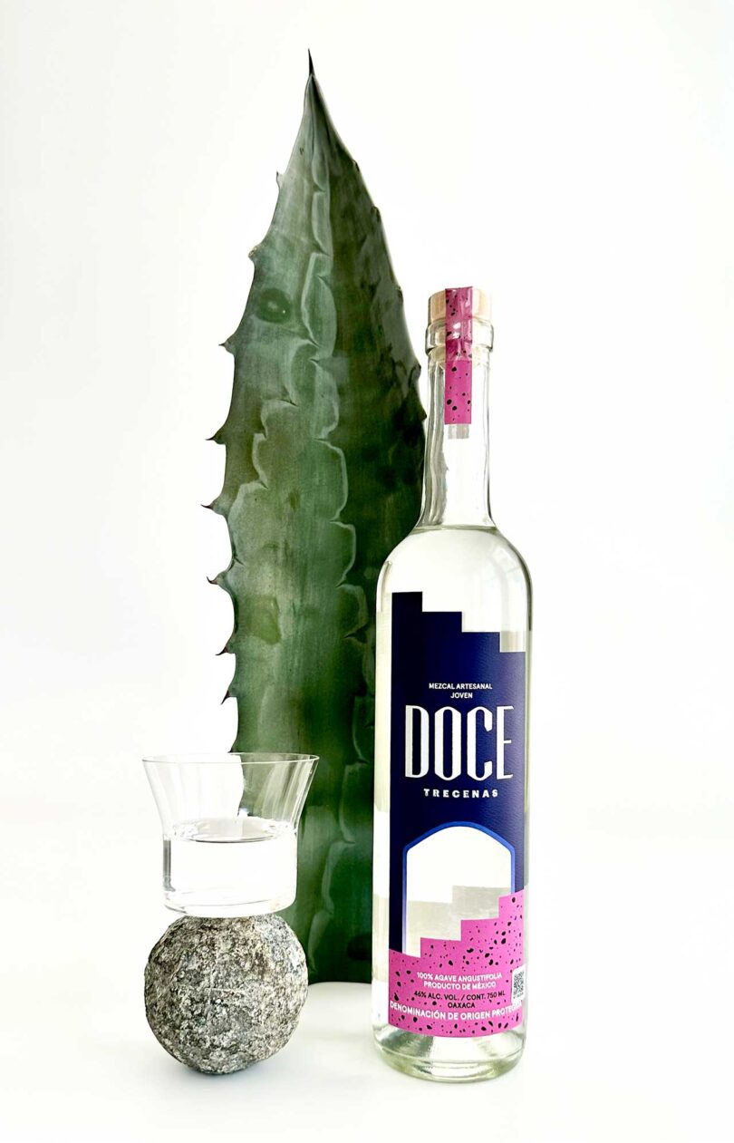 bottle of Doce Mezcal next to shot glass with agave leaf in back