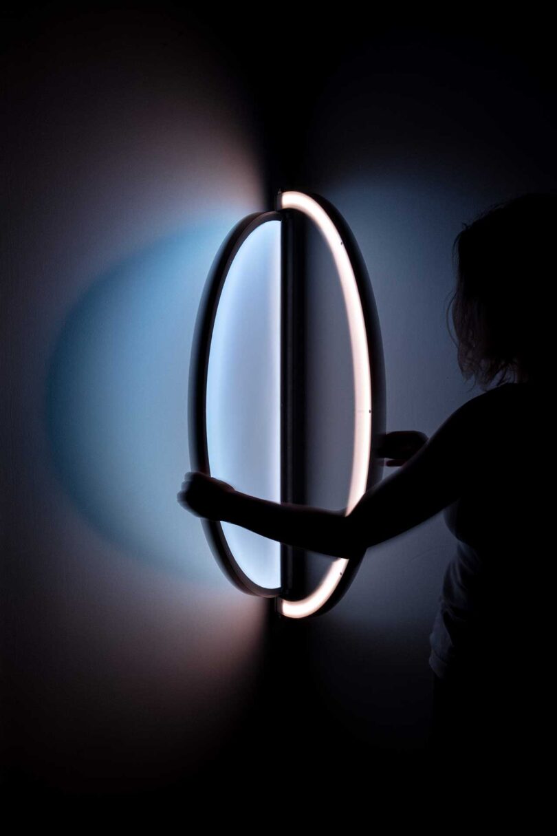a person hanging an oval-shaped wall light that resembles a window when illuminated