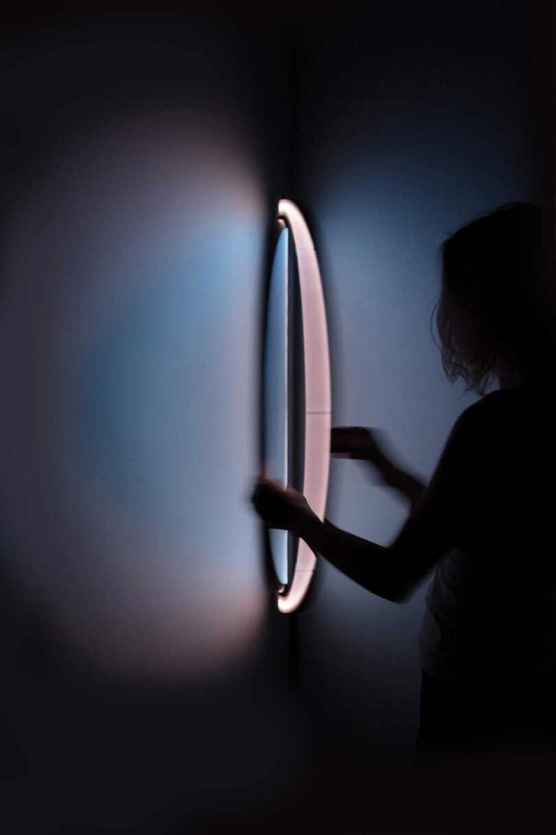 a person hanging an oval-shaped wall light that resembles a window when illuminated