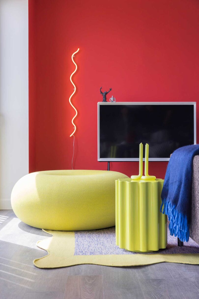 partial interior shot of a modern living room full of primary colors including a red wall, yellow donut pouf