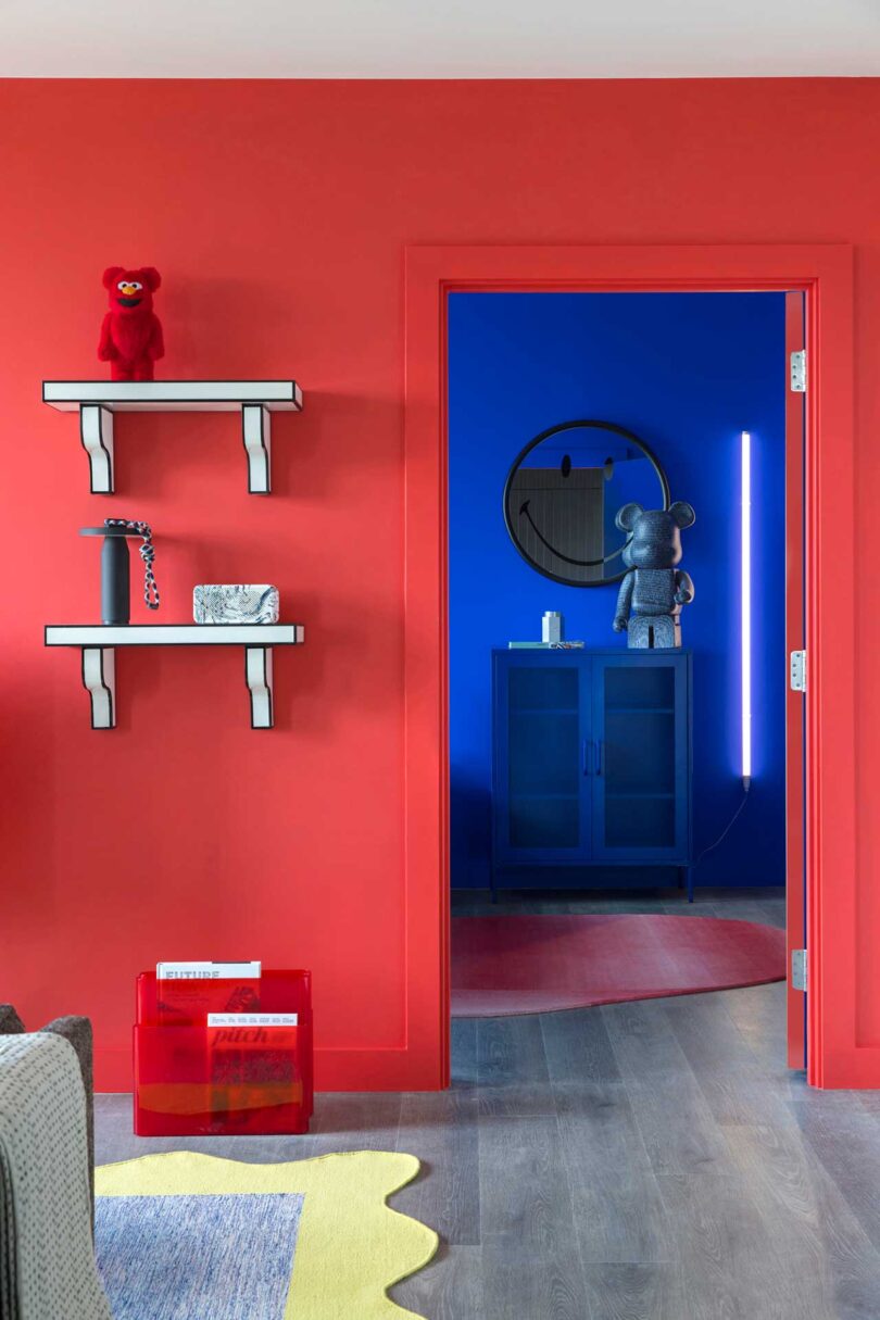 interior view of modern apartment looking past red wall with cartoon shelves into cobalt blue bedroom