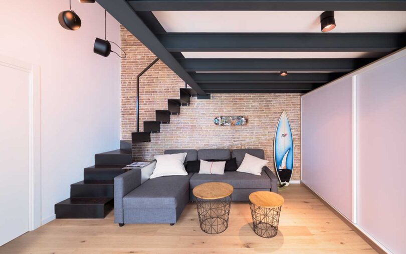 interior view of modern living space with small sectional sofa underneath loft bed with stairs wrapping around