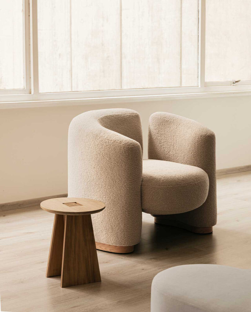 upholstered modern armchair with low wood stool next to it
