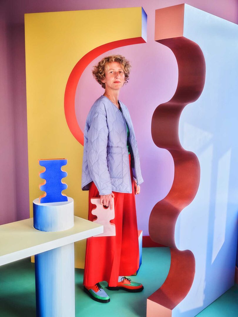 artist Pani Jurek standing sideways amongst colorful vases and vibrant space