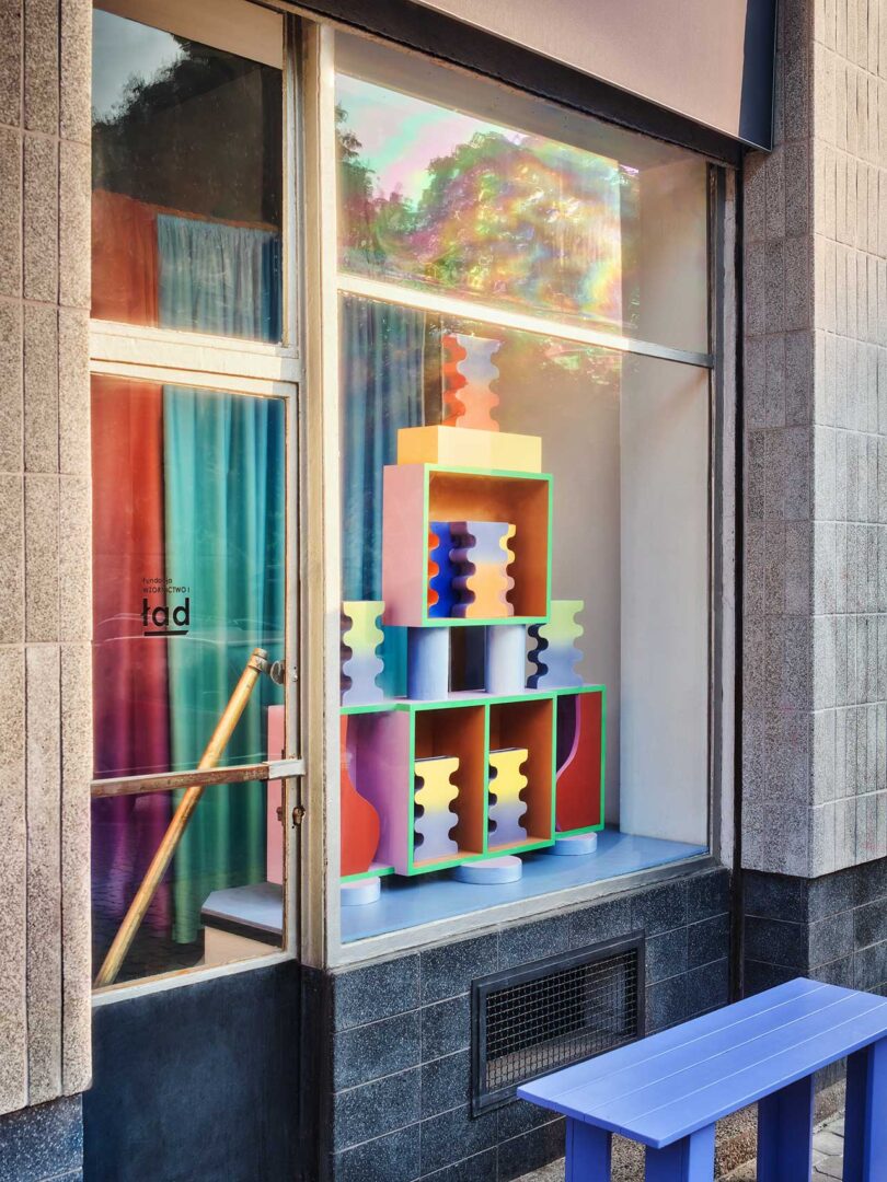 angled storefront view of gallery with colorful window display of stacked abstract colorful vases.