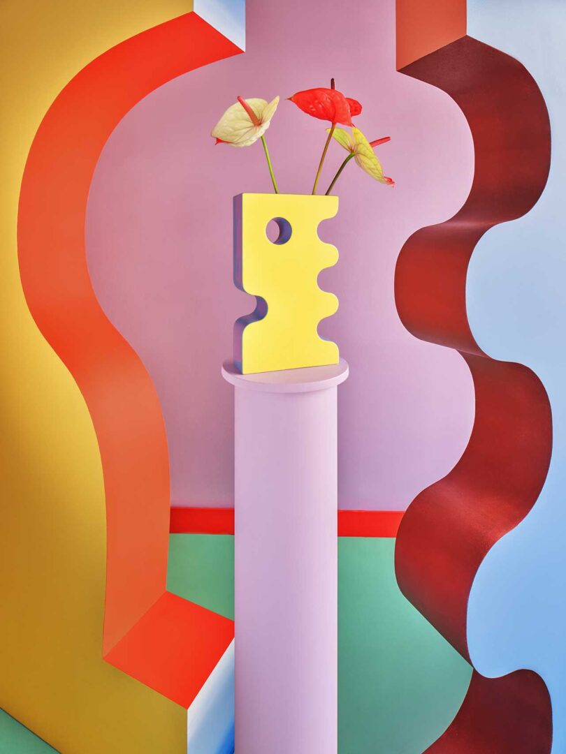 lavender column holding a unique blue and yellow abstract vase with curved colorful walls beside it