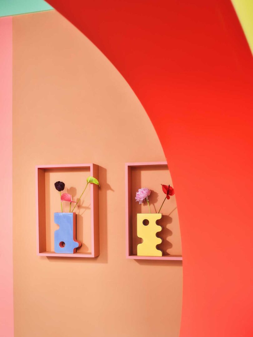 looking under red archway to a peach wall with two frames holding abstract vases
