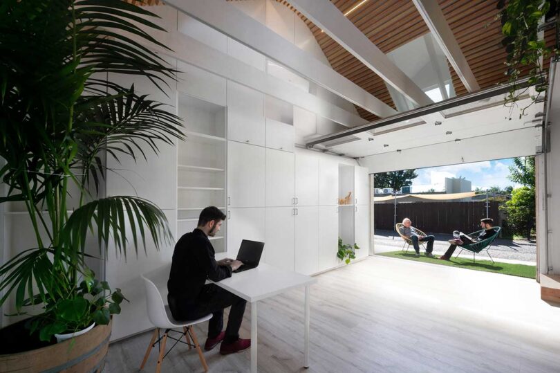 angled interior view of renovated garage with man sitting at foldout desk from wall of cabinets with garage door open