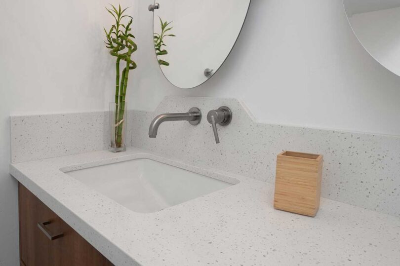 angled closeup of simple bathroom counter with round mirror above