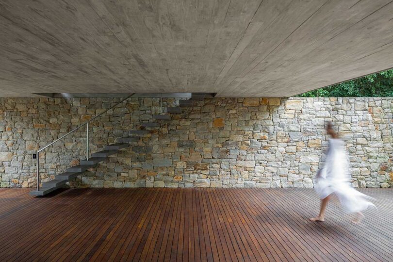 Terraza de madera cubierta con escaleras flotantes que se elevan por un muro de piedra