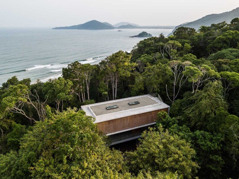 sky view looking down at modern house surrounding by trees with ocean in distance