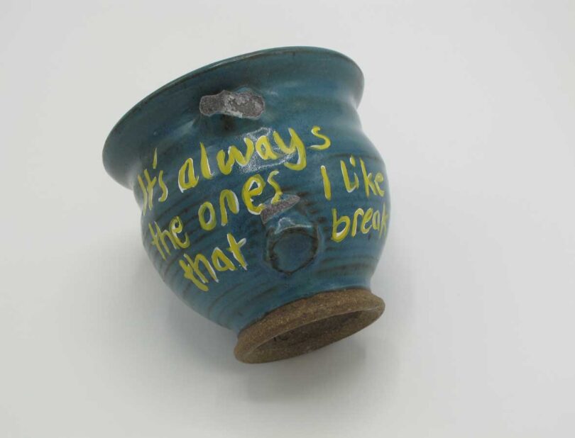piece of blue pottery laying down with yellow writing on it