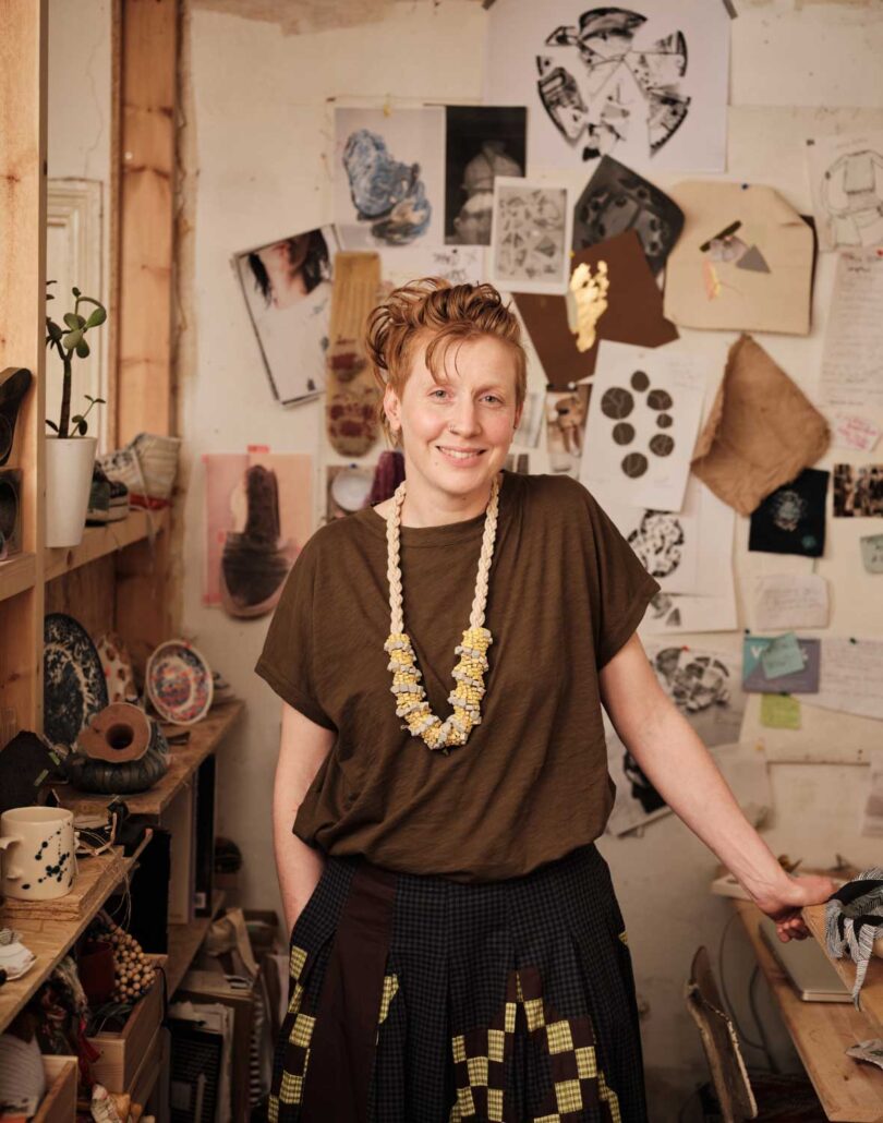 red-headed person standing in front of inspiration wall wearing brown shirt and necklace