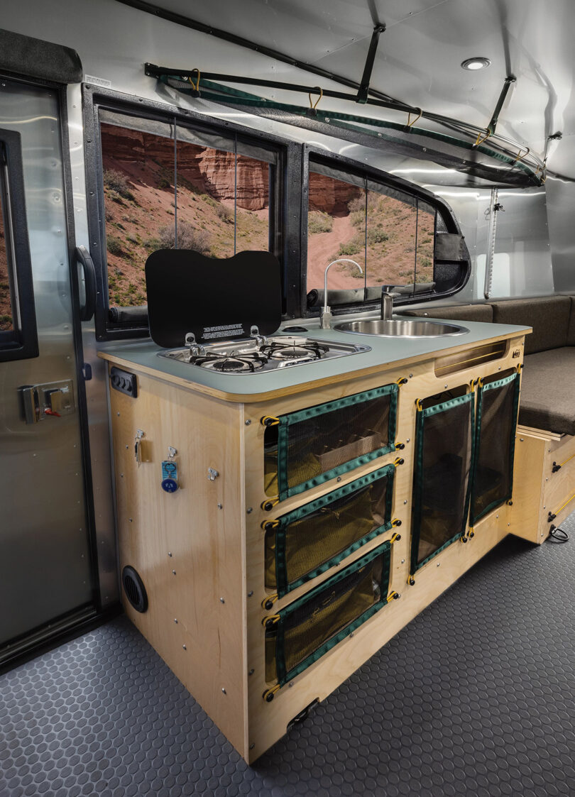 Angled view of the multi-layered green slate countertop, adorned with exposed birch plywood within the REI Edition Airstream, with burners cover lifted.