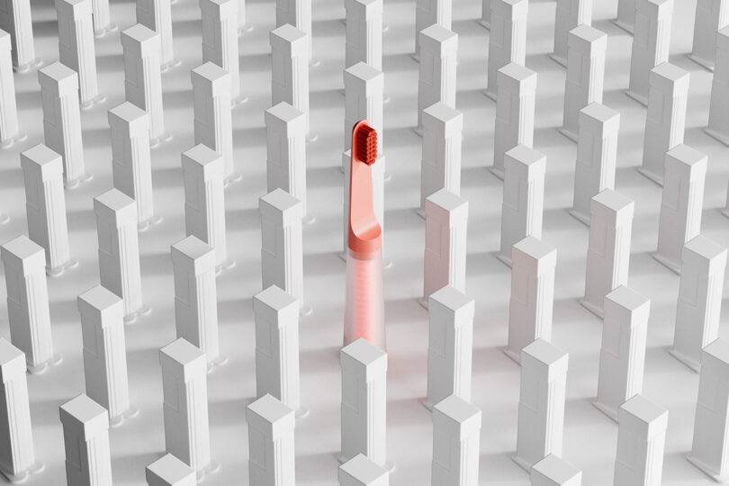 One coral colored one&done toothbrush standing in the center of a grid work of white columns.