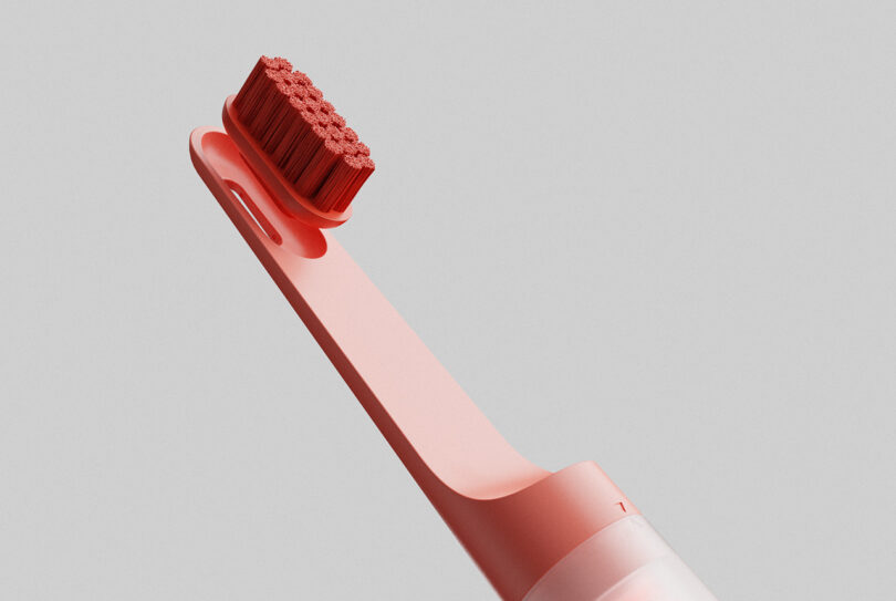 Detail of the coral red toothbrush with replacement head partially removed.