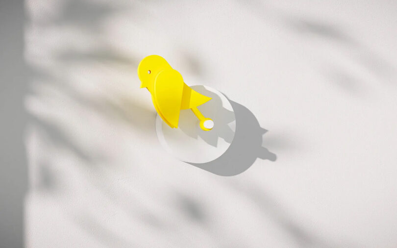 Monitor de qualidade do ar em forma de pássaro amarelo passarinho na posição vertical instalado em uma parede, mostrando uma ligeira diminuição da qualidade ideal do ar interno.