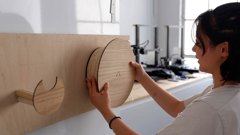 Woman holding a wood prototype of the Cove's primary charging unit installed onto a wall used to review its size and shape, with smaller charging plug holder also in wood to the left.