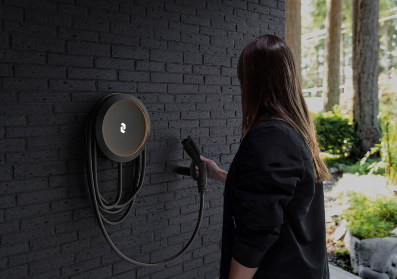 Woman with long dark hair in black top reaching to either remove Cove charging port from wall mounted holder.