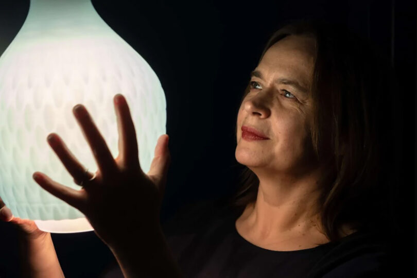 Aleksandra Gaca holding an illuminated Philips Droplet Three Pendant light in both hands, with light softly glowing across her face.