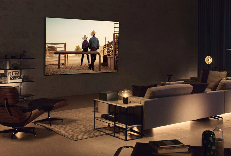 Nighttime setting of modern living room space with smaller 77-inch LG SIGNATURE OLED M with cowboy son and father seated viewed from the back on the screen. Ambiance of living room is dim warm lights.