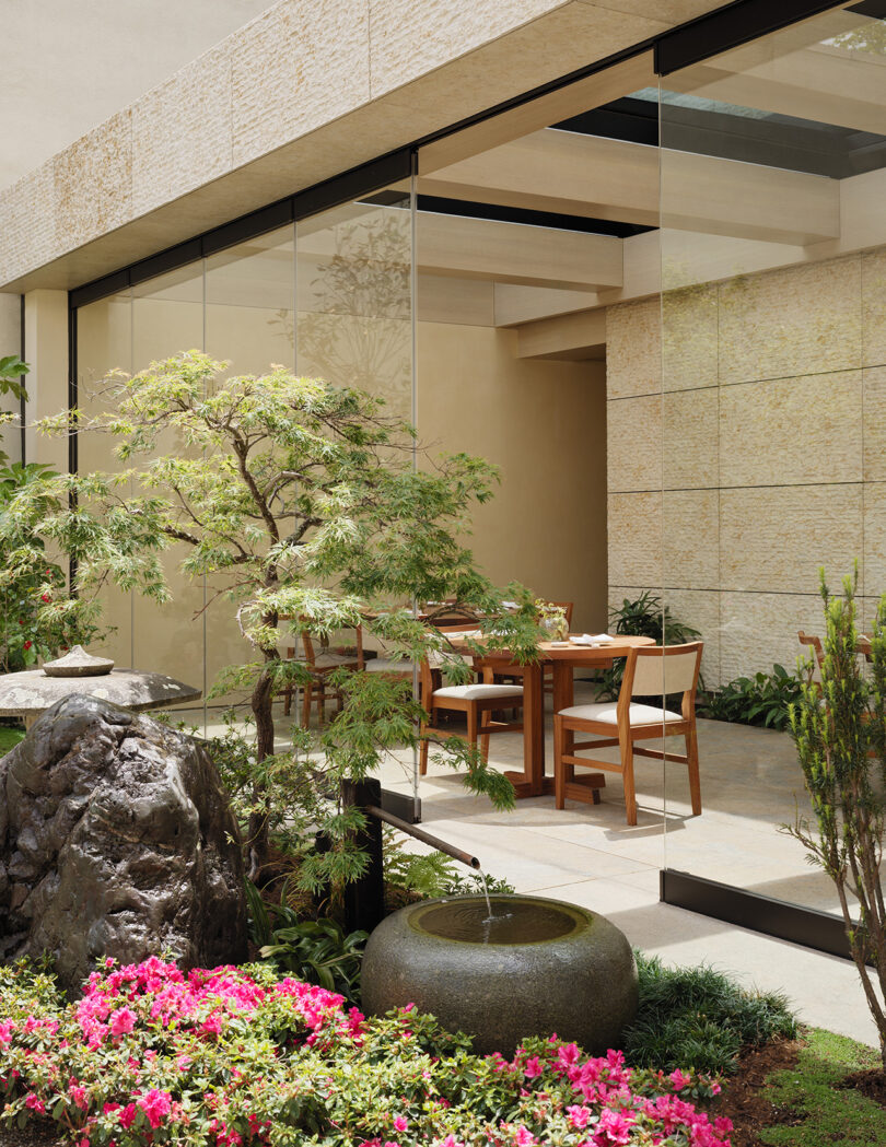 View from Nobu Hotel Palo Alto Japanese garden looking into dining area, with two dining tables visible in the background and a Japanese bamboo water fountain in the foreground.