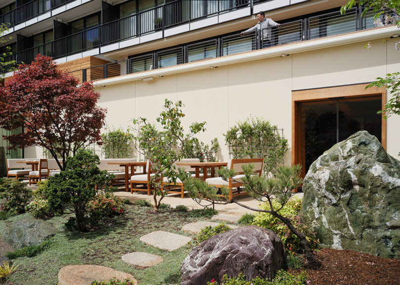 Man leaning over railing surveying Nobu Hotel's Japanese rock garden landscaped with California native plants and outdoor dining furniture.