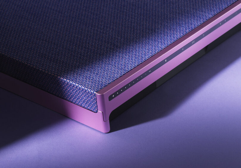 Detail corner of Fall 2023 Atelier Editions Beosound Level wireless speaker in Lilac Twilight color staged against a purple floor and background with shadows cast across it showing where the aluminum pink frame meets the speaker fabric front.