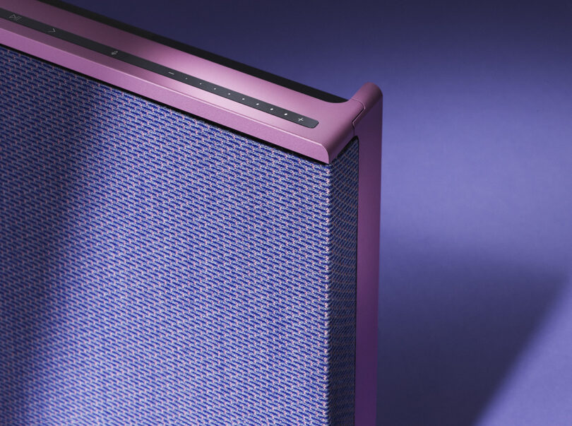 Detail top right corner of Fall 2023 Atelier Editions Beosound Level wireless speaker in Lilac Twilight color staged against a purple floor and background with shadows cast across it showing where the aluminum pink frame meets the speaker fabric front.
