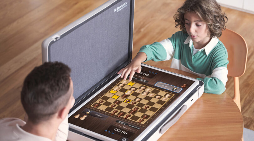 Young man and young boy playing chess video game on the screen of the LG StanbyME Go open with the 27-inch LED display in flat position.