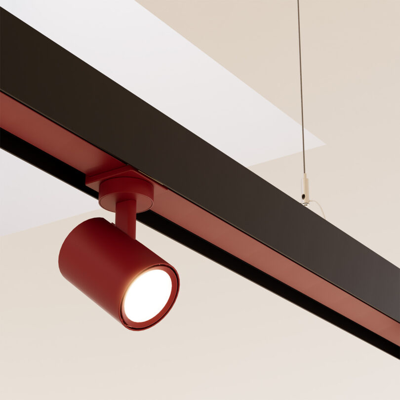 Red suspension ribbon track with one spot light attachment hanging from ceiling. Light is pointing toward the bottom right at an angle.