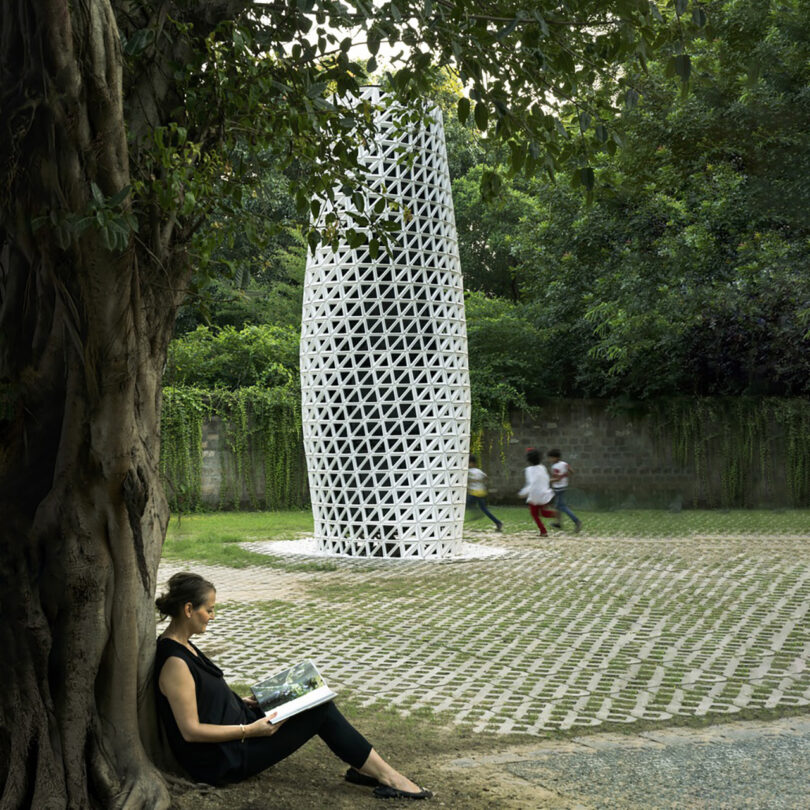 Woman sitting under and against a tree with VERTO air purifier tower in the background in a park setting, with three children running behind it as a blur.
